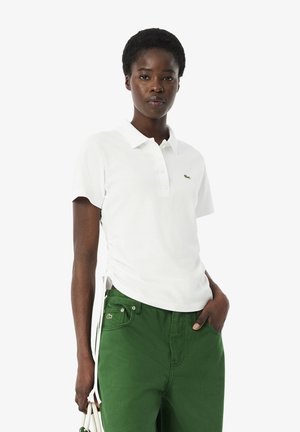 White polo shirt made of cotton, featuring a classic collar, short sleeves, and a green embroidered logo on the chest. Paired with green pants.