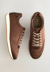 Bruna syntetiska sneakers med en slät yta, kontrasterande beige snören, vit sula och en rundad tådesign. Logotypen synlig inuti.