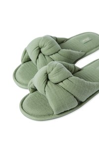 Pantofole di stoffa verdi con un design annodato su ciascun cinturino, superficie morbida al tatto, soletta imbottita e suole arrotondate.