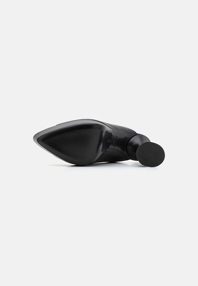 Black high-heeled shoe with a pointed toe and smooth texture. The sole is flat with a circular accent on the heel.
