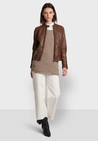 Bruine leren bomberjack met een ritssluiting, gelaagd over een lichtbruin sweater, gecombineerd met witte wijde broek en zwarte enkellaarsjes.