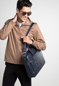 Borsa messenger in pelle blu navy con doppi manici superiori e tracolla regolabile, dotata di tasca anteriore e finitura testurizzata.