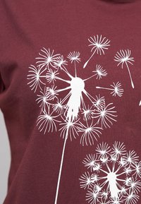 Bordeaux t-skjorte med en hvit dandelion-grafikk, som har fine linjer og kronblader, som skaper et naturlig, strukturert utseende.