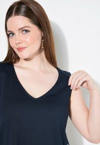Top azul marino de cuello en V con mangas cortas, hecho de una tela suave, con un corte relajado y una textura sutil. Los pendientes tienen un diseño estampado.