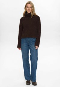 Rjava, teksturirana pulover s turtleneckom in dolgimi rokavi, v kombinaciji z modrimi, visokimi jeans hlačami in rjavo obutvijo. Preprost, vsakdanji outfit.