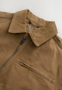 Bruine zip-up jas met een corduroy kraag, voorzien van een voorzak en een zachte, textuurvolle stof. Strak geknipt zonder extra details.