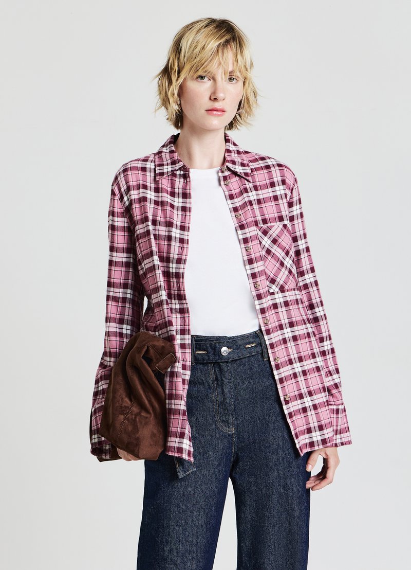 Camicia di flanella a quadri rosa e bianca, abbottonata, con taschino sul petto, abbinata a una maglietta bianca e pantaloni in denim scuro a vita alta.