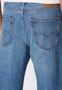 Lyseblå denimbukser med løs passform, som har baklommer, kontrasterende sømmer og et lærhode på linningen.