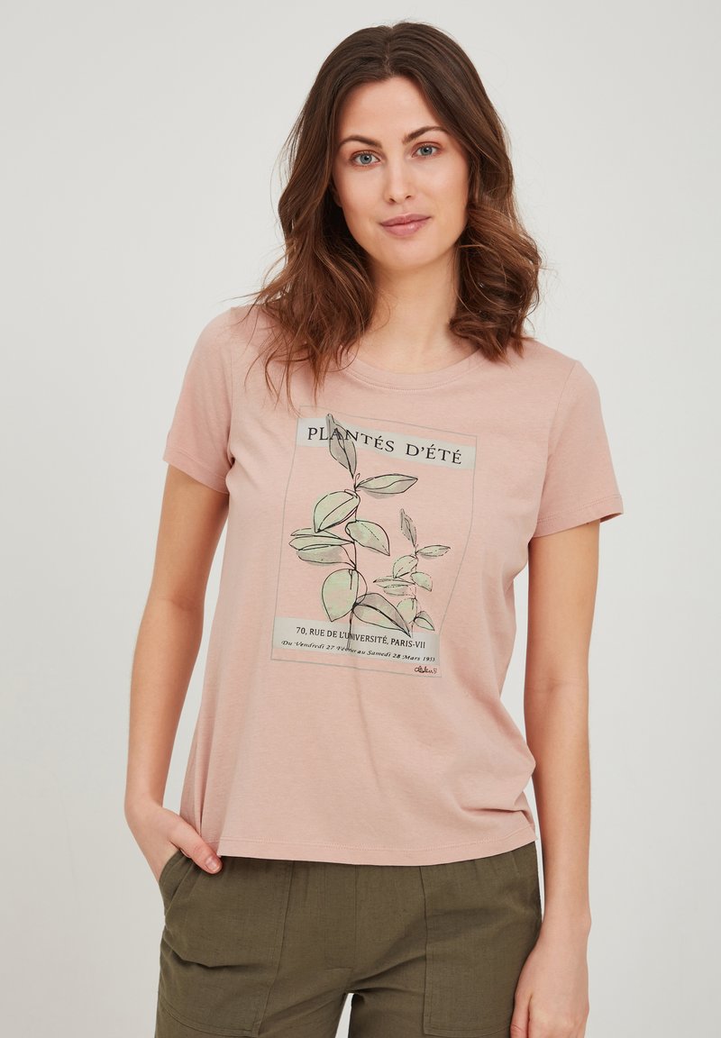 Camiseta de manga corta color rosa claro, hecha de una tela suave, con un estampado botánico que incluye texto en francés en verde y negro. Corte sencillo y relajado.