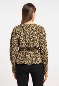 Blúzka s leopardím vzorom v zemitých tónoch, s úzkym pásom, dlhými rukávmi a voľným strihom. Tkanina má hladkú textúru.