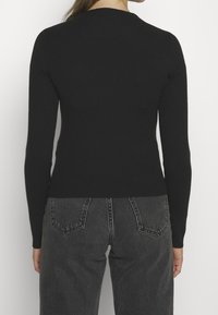 Svart ribbad tröja med långa ärmar, rundad halsringning och en figurnära silhuett. Matchad med högmidjade grå jeans.