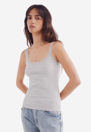 Grijze tanktop van zacht ribbelstof. Heeft een kantafwerking langs de halslijn en schouderbanden, met een kleine strikdetails aan de voorkant.