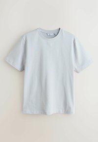 T-shirt gris clair à manches courtes et col rond, suspendu devant un fond neutre uni, taille moyenne avec étiquette de la marque visible à l'intérieur du col.