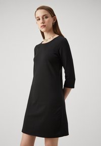 Svart skiftklänning i slät tyg, med trekvartsärmar och rund halsringning, med en minimalistisk design utan utsmyckningar.