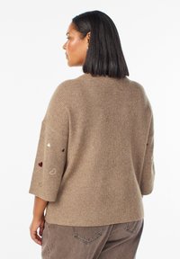 Maglione marrone a coste con maniche a tre quarti e cuori ricamati in rosso e bianco ai polsini, tessuto a maglia texture.