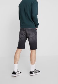 Mustat denim-shortsit, joissa on haalistunut muotoilu, taka-taskut ja suora leikkaus, yhdistettynä ruudullisiin lenkkareihin ja valkoisiin nilkkasokkeihin.