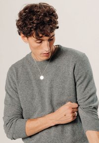 Grauer Pullover aus weichem Material, mit Rundhalsausschnitt, gerippten Bündchen und lockerer Passform. Sichtbare Silberanhänger-Halskette.