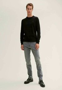Black long-sleeve sweater paired with light gray jeans and black dress shoes. The outfit features a simple design and fitted shape.