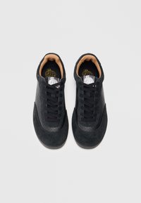 Zapatillas negras con un diseño de ante y perforaciones, presentan cordones negros, suela de goma negra y un forro interior marrón.
