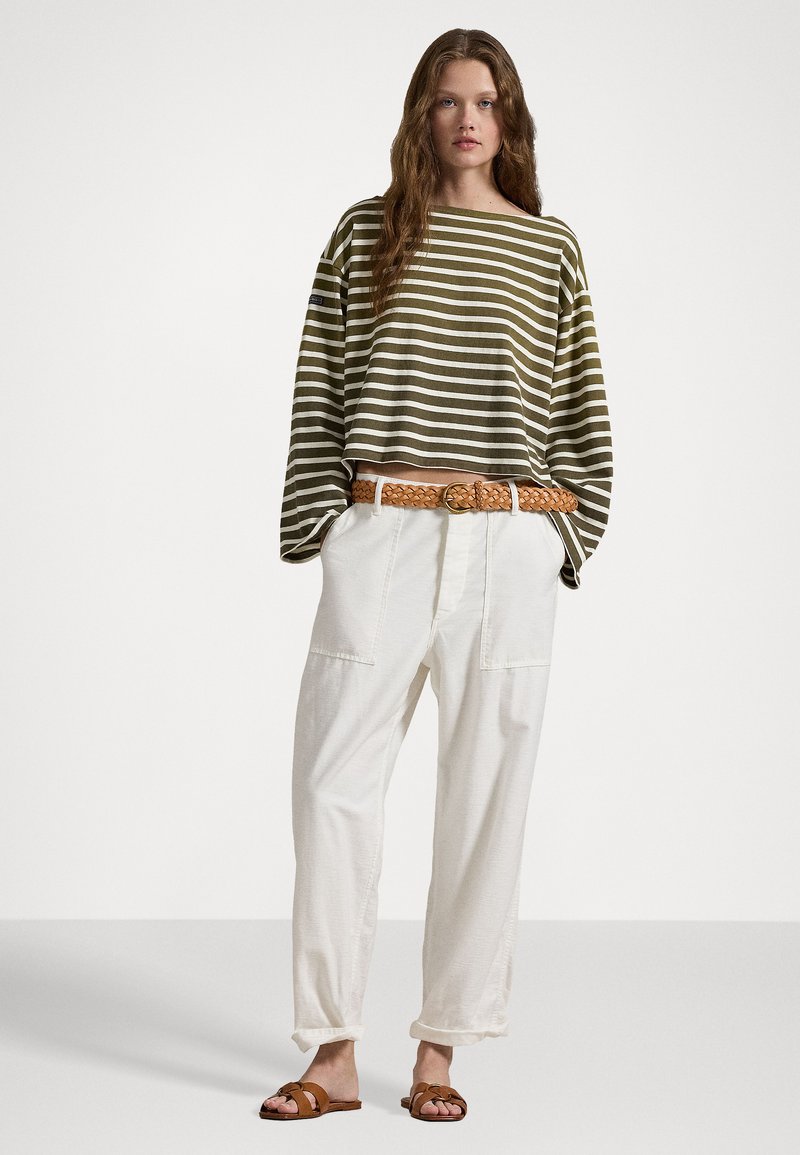 Beige und weiße gestreifte oversized Langarmbluse, kombiniert mit weißen locker sitzenden Hosen mit Taschen und einem geflochtenen braunen Gürtel. Braune Sandalen.