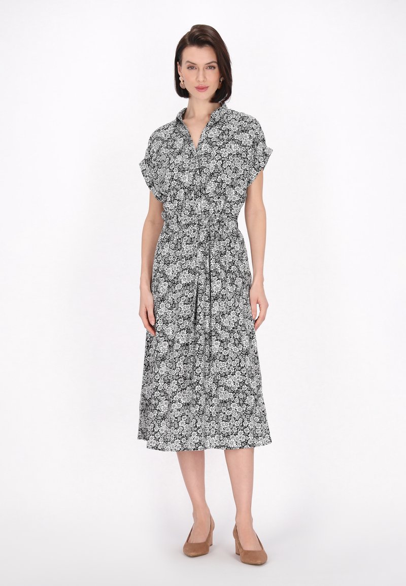 Rochie midi cu flori alb-negru, cu mâneci scurte, talie strânsă și curea, având guler și o textură fluidă. Pantofi cu toc bej.