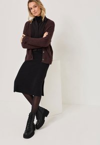 Cardigan bordeaux avec des boutons sur un haut et une jupe noirs. Des collants noirs et des bottines à lacets épaisses complètent le look. Design simple et texturé.