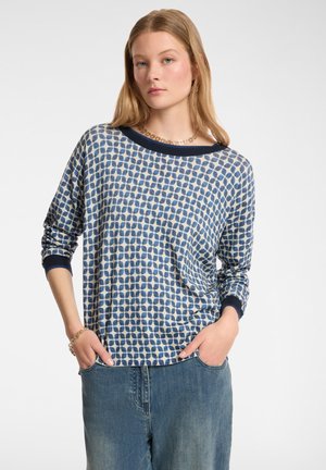 Maglietta a maniche lunghe blu e crema con un ampio scollo, abbinata a jeans a gamba larga azzurri.