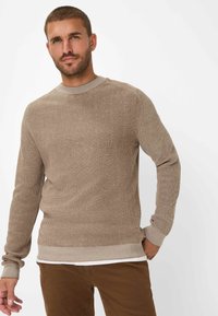 Beige ribbed knit sweater with a crew neckline, ribbed cuffs, and waistband. Worn over a white t-shirt, paired with brown pants.