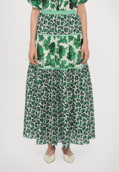 Falda maxi con un estampado floral verde sobre un fondo claro. Presenta una cintura fruncida y un dobladillo con volantes. Se lleva con zapatos de punta beige.