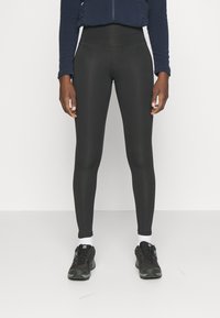 Leggings negros de material elástico, de cintura alta, con una textura suave. Combinados con zapatillas deportivas negras y calcetines blancos.