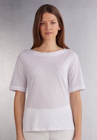 Maglietta bianca a maniche corte con scollo rotondo, texture liscia e polsi arrotolati, dal taglio morbido e senza motivi o accessori visibili.
