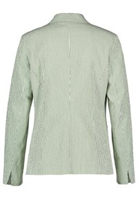 Veste rayée verticalement verte et blanche avec des manches longues, un col pointu et une coupe ajustée. Présente une texture subtile et des fentes latérales.