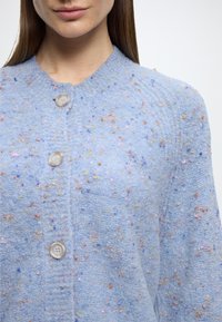 Casaco azul claro feito de material texturizado, com manchas multicoloridas, decote redondo e três botões frontais para fechar.