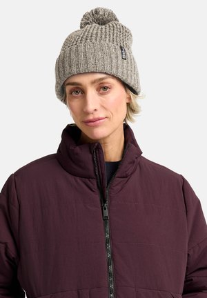 Beanie grigia lavorata a maglia con texture a coste e pom-pom sulla parte superiore, abbinato a una giacca imbottita bordeaux con chiusura a zip e colletto alto.