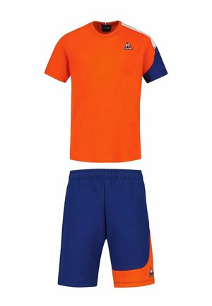 Camisa de manga corta naranja con detalles azules, combinada con pantalones cortos azules que presentan un panel naranja. Hecho de tela suave, diseño informal para mayor comodidad.