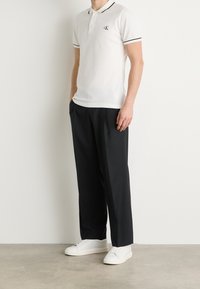 Vit polo skjorta med svarta detaljer och logotyp på bröstet, kombinerad med lösa svarta byxor och vita sneakers. Mjuk tyg, avslappnad passform.
