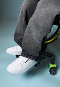 Valged ketsid siledast materjalist ja paeltega, paaritatud hallide, veidi kulunud pükstega, paigutatud ratastooliratta peale.