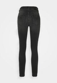 Jean skinny noir taille haute avec poches arrière et détails de coutures, présenté sur un fond blanc uni.