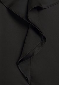 Černá látka s měkkou, hladkou texturou a ozdobným řasením na okraji. Řasení je jemně zakroucené na lemu, což vytváří jemný pohyb v designu.