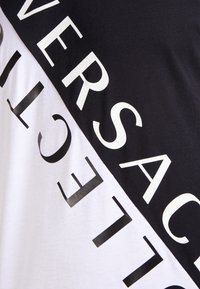 Czarny i biały t-shirt z przekątnym podziałem i wyróżniającym się, graficznym tekstem w kontrastowych kolorach na każdej połowie. Miękka bawełniana tekstura.