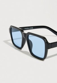 Μαύρα ορθογώνια γυαλιά ηλίου με μπλε φακούς, με χοντρό σχεδιασμό και υφή στο πλαίσιο. Ετικέτα "PIER ONE" στον βραχίονα.