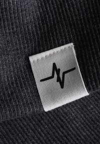 Dunkelgrauer Strickstoff mit einer strukturierten Oberfläche. Ein rechteckiges weißes Etikett zeigt ein stilisiertes schwarzes Herzschlag-Symbol.