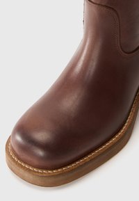 Brauner Lederstiefel mit runder Zehenform, glatter Textur und sichtbaren Nähten, ausgestattet mit einer leicht erhöhten Gummisohle.
