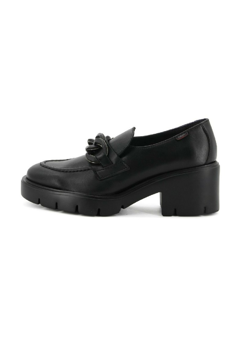 Mocasín de cuero negro con tacón robusto, suela gruesa estriada y detalle decorativo de cadena en la parte superior, mostrado sobre fondo blanco.