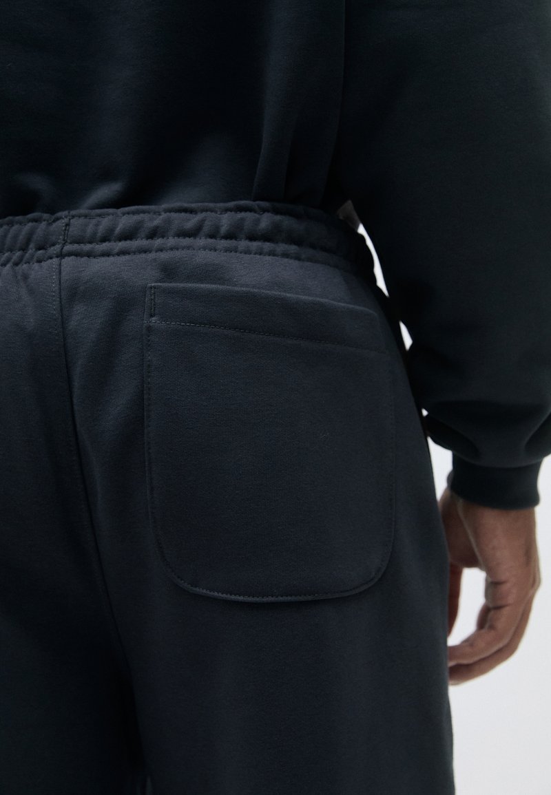 Mørkegrå sweatpants med en baglomme, elastisk talje og blød stoftekstur. Minimalistisk design med enkle syninger.