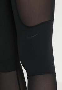 Leggings sportivi neri con pannelli in rete, realizzati in tessuto elasticizzato, con una vestibilità aderente e un piccolo logo Nike nero vicino alla coscia superiore.