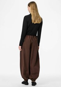 Czarna bluzka z długim rękawem, brązowe luźne spodnie z talią marszczoną i elastycznymi mankietami, w połączeniu z czarnymi płaskimi butami.
