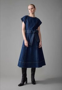 Sukienka dżinsowa w ciemnym niebieskim kolorze, z krótkimi rękawami, taliowana w pasie i z rozkloszowaną spódnicą. Charakteryzuje się widocznymi przeszyciami i bocznymi kieszeniami.