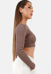 Brauner gerippter Crop-Top mit langen Ärmeln, mit einer taillierten Passform und weichem Material. Kombiniert mit hochgeschnittenen weißen Jeans.