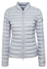 Ljusgrå puffjacka med ståkrage, baktill dragkedja, quiltat mönster och slät, glänsande yta. Har en liten logotyp på ärmen.
